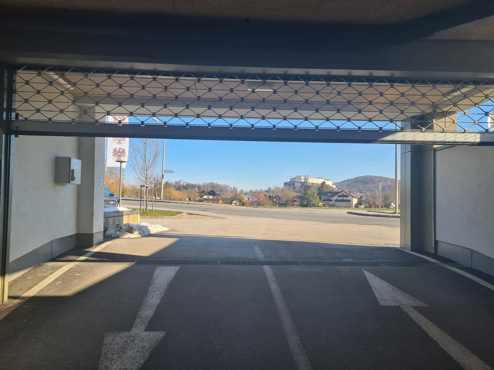 Blick aus der Tiefgarage auf die sonnige Umgebung mit Häusern und grünen Hügeln.