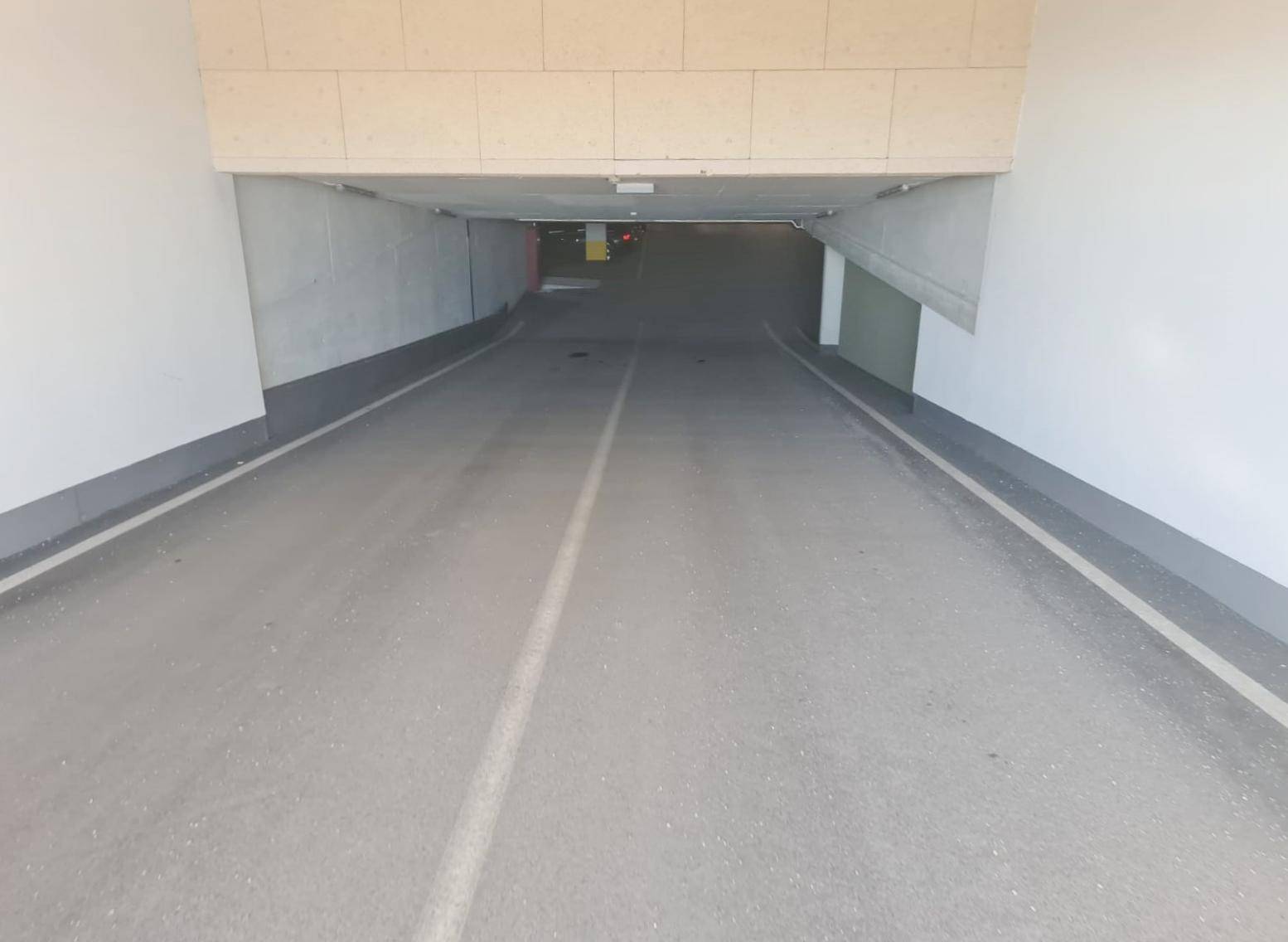 Einfahrtsrampe zur Tiefgarage mit klaren Markierungen und guter Beleuchtung, die in den Untergrund führt.