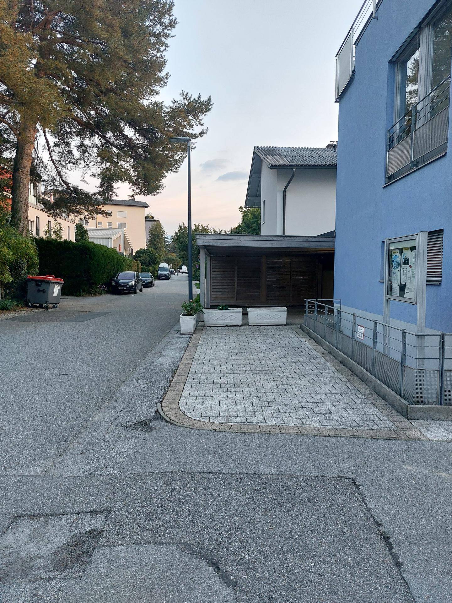 Außenansicht des modernen Gebäudes mit gepflastertem Parkplatz, Rampe und umliegender Wohngegend.