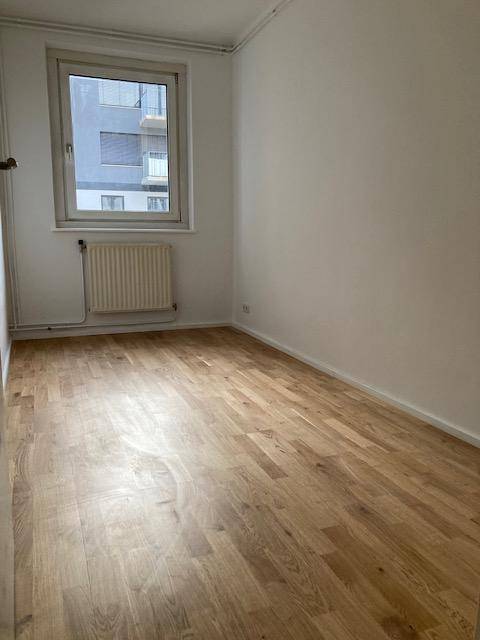 Ruhiges Zimmer mit Parkettboden, weiß gestrichenen Wänden und Blick nach draußen.