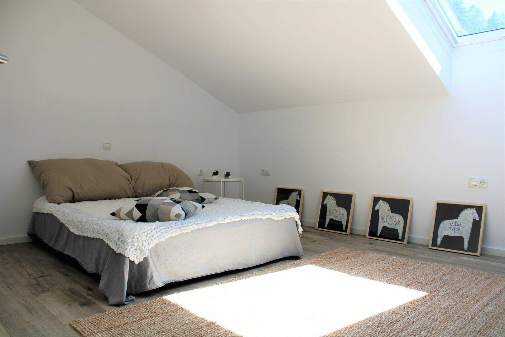 Gemütliches Schlafzimmer im Dachgeschoss mit Holzboden und großem Dachfenster.