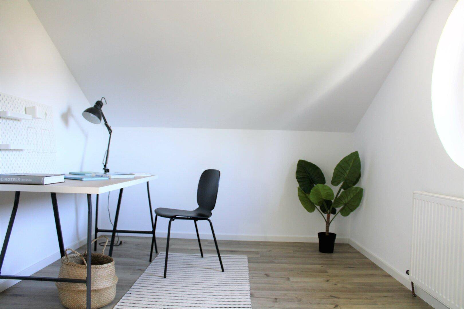 Ruhiges Arbeitszimmer im Dachgeschoss mit Schreibtisch, Pflanze und Dachschräge.