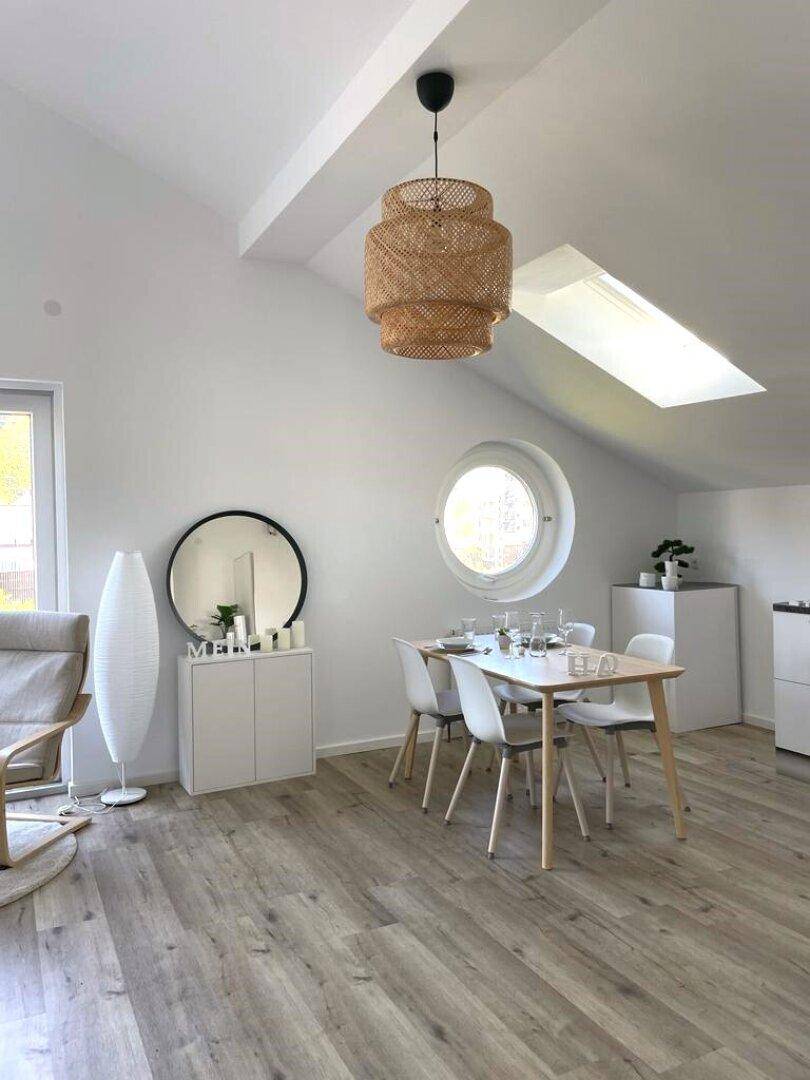 Heller Essbereich mit Holzboden, runden Fenstern und moderner Hängelampe.