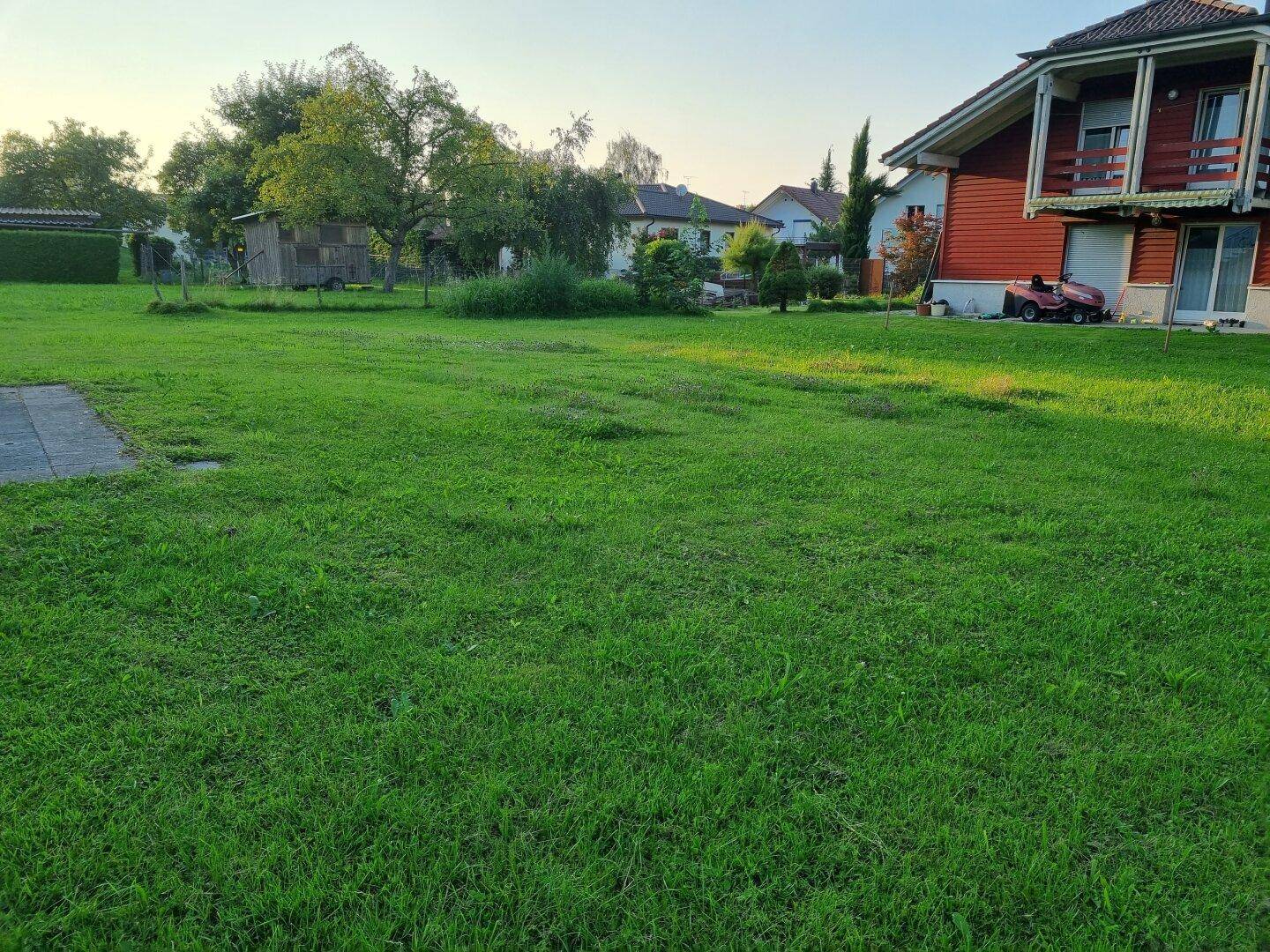 Weitläufiger Garten mit Rasenfläche, angrenzendem Wohnhaus und einem Rasenmäher.