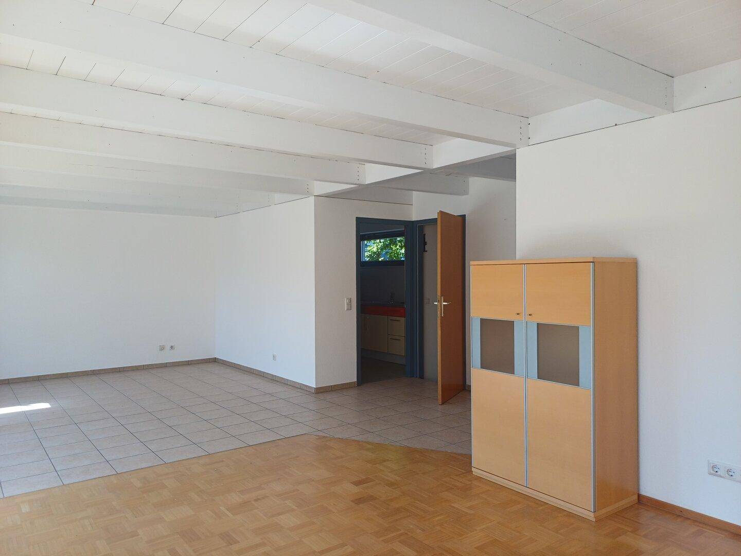 Geräumiger Wohnbereich mit sichtbaren Holzbalken, gemischtem Fliesen- und Parkettboden und viel Tageslicht.