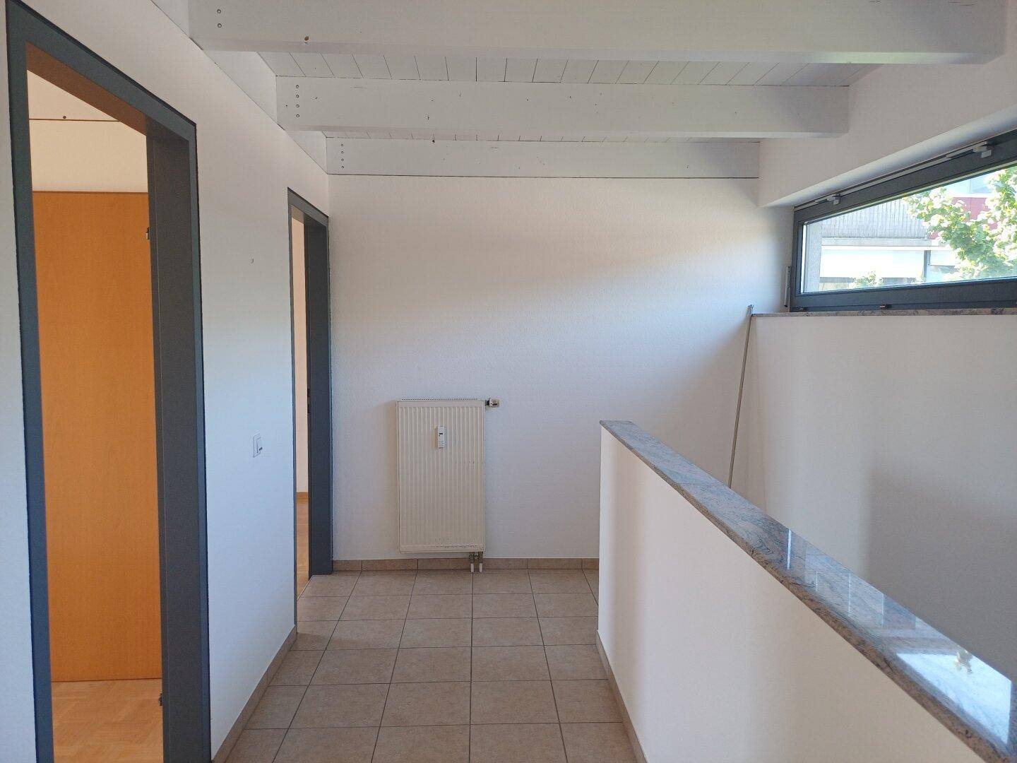 Heller Flur mit Fliesenboden, Heizkörper und einem Fenster, das für natürliche Belichtung sorgt.
