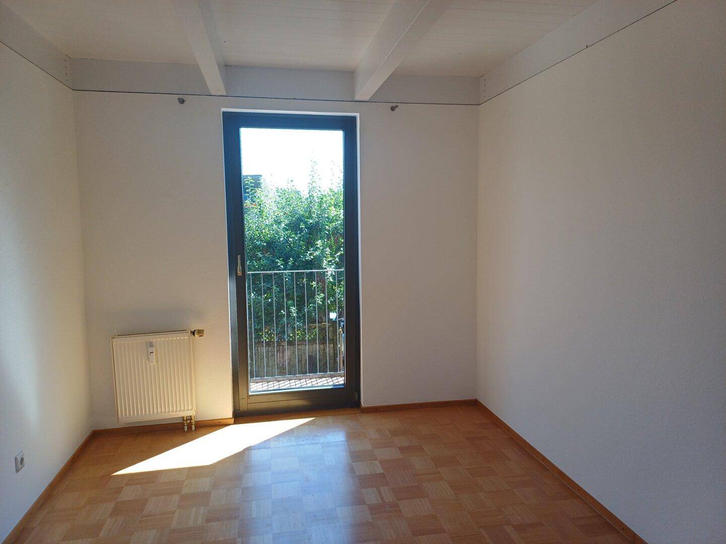 Helles Schlafzimmer mit Parkettboden und einer Tür, die zu einem französischen Balkon führt.