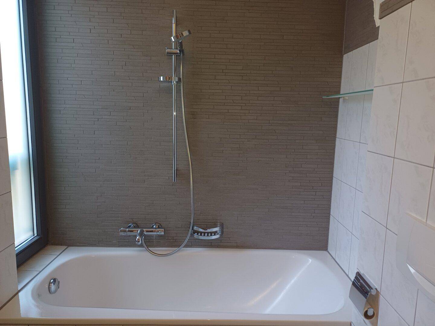 Badezimmer mit Badewanne, integrierter Duscharmatur und modernen grauen Wandfliesen.