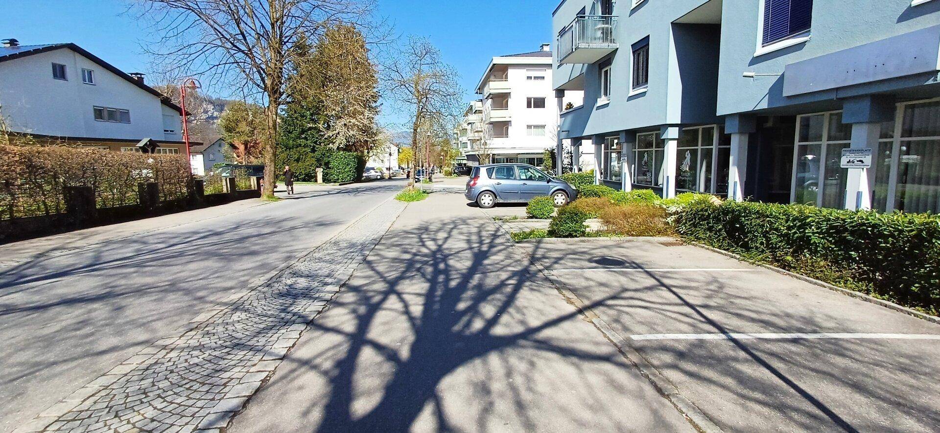 Blick auf die Straße mit dem Gebäude, weiteren Häusern und einem geparkten Auto unter blauem Himmel.