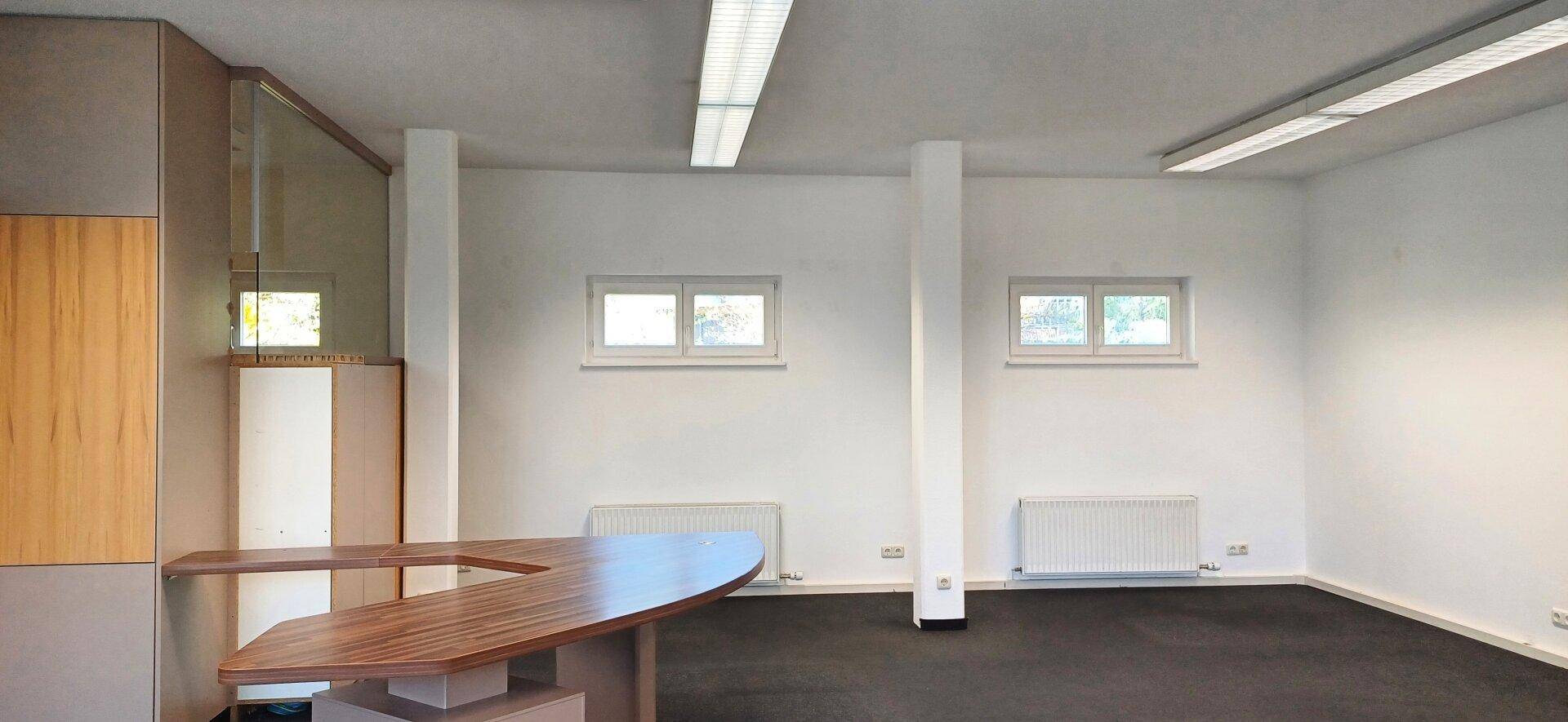 Heller Büroraum mit dunklem Teppichboden, weißen Wänden und integrierten Holzmöbeln.