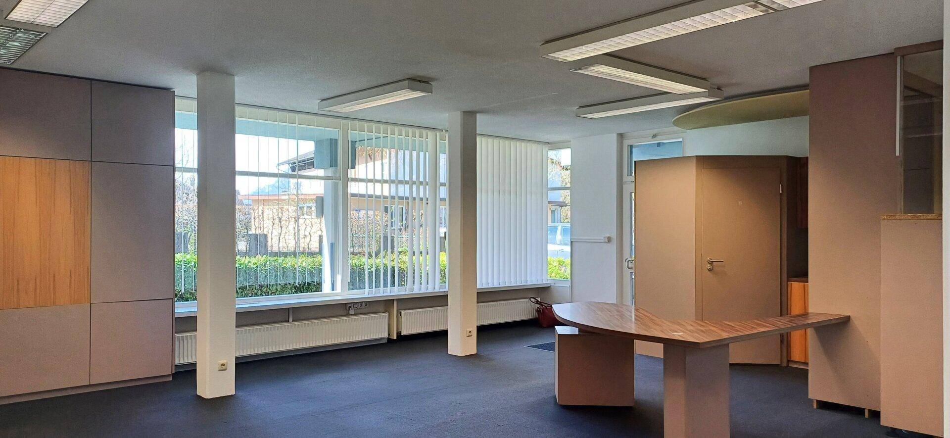 Geräumiger Bürobereich mit großen Fenstern, vertikalen Jalousien und funktionalen Einbaumöbeln.