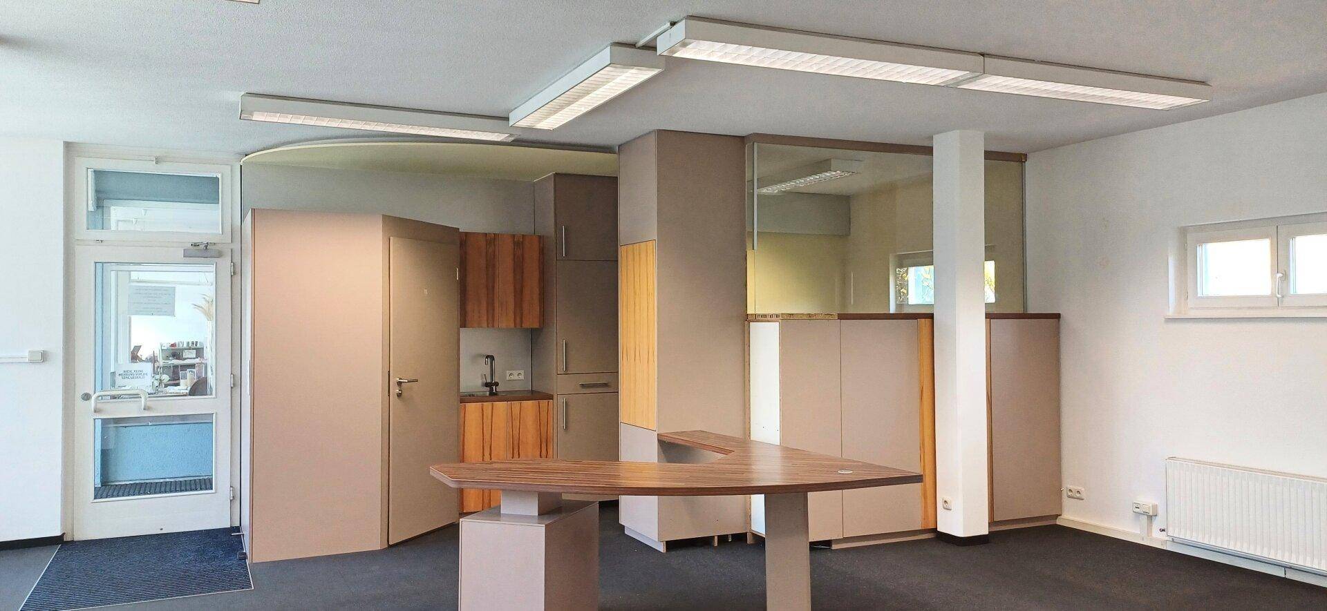 Bürofläche mit integrierter Küchenzeile und modernem Schreibtisch, gut beleuchtet durch Tageslicht.