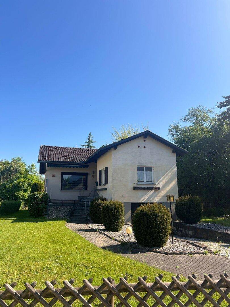 Freistehendes Einfamilienhaus mit Satteldach, Vorgarten und umgebender Natur an einem sonnigen Tag.