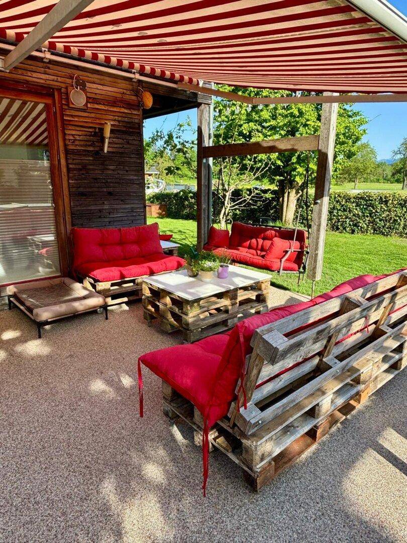 Gemütliche Terrasse mit Palettenmöbeln und roter Markise, ideal für entspannte Stunden im Freien.