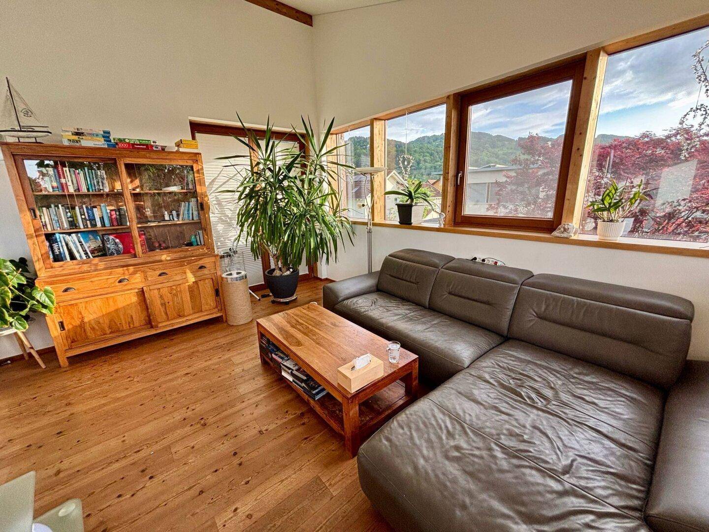 Gemütliches Wohnzimmer mit Holzboden, Ledersofa und Bücherregal, bietet einen weiten Blick ins Grüne.