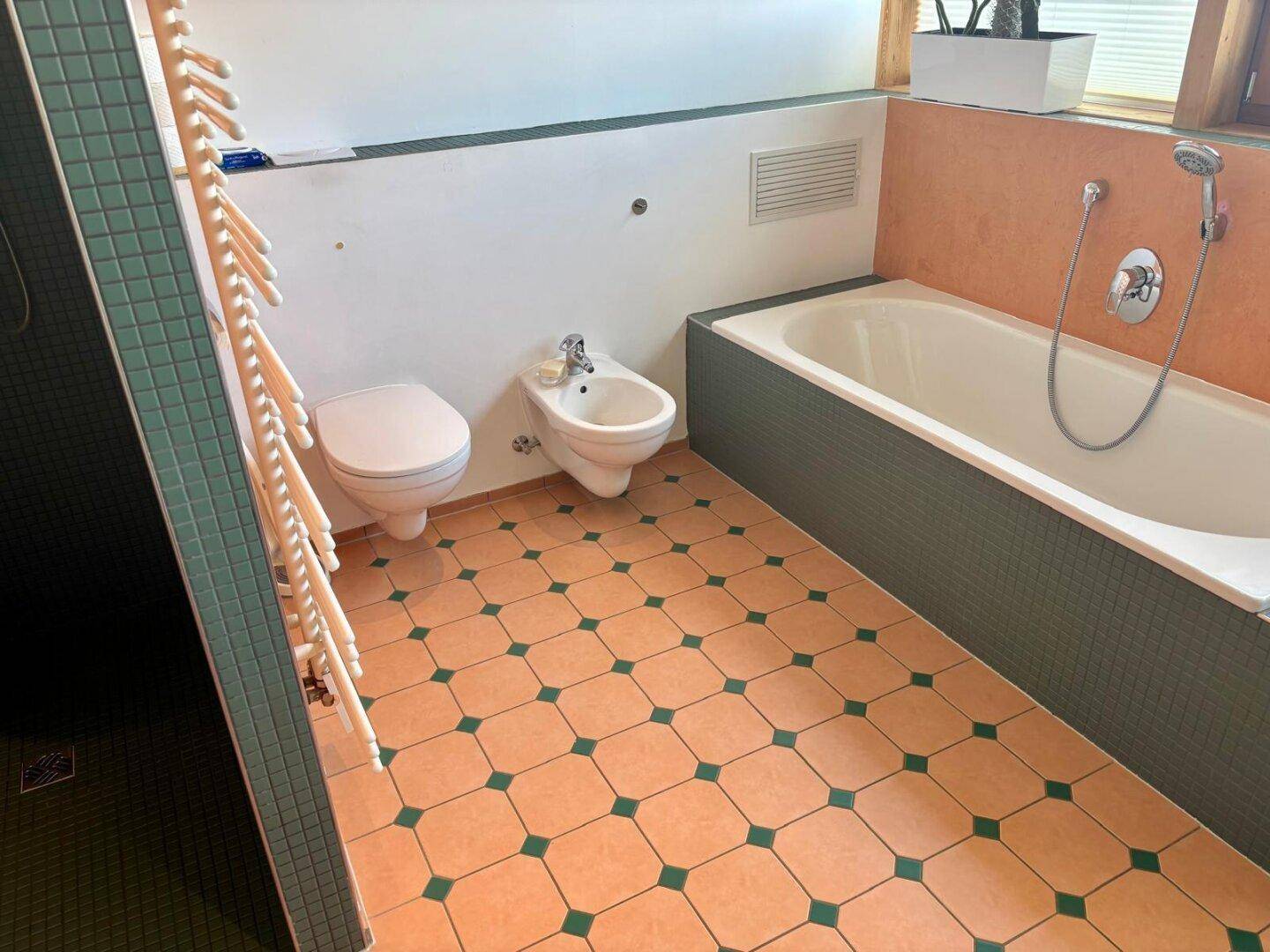 Badezimmer mit Badewanne, Bidet und farbigen Fliesen, ausgestattet mit einem Handtuchheizkörper.