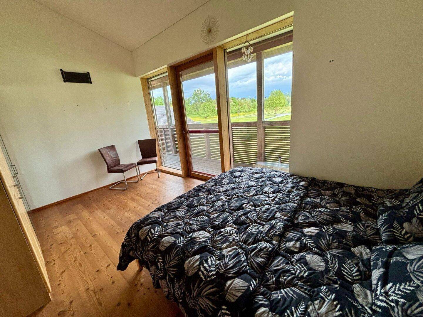 Schlafzimmer mit Holzboden und großem Schiebefenster, das Zugang zu einem Balkon bietet.