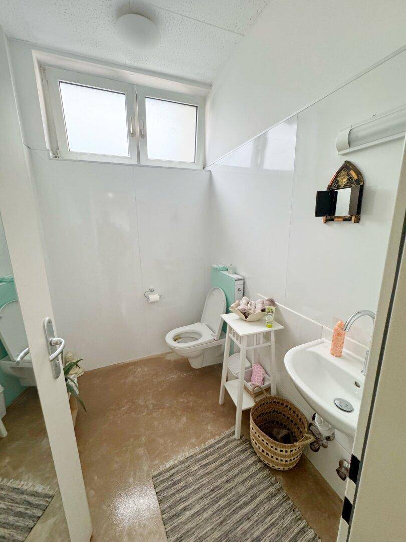 Helles Gäste-WC mit Fenster, Toilette und kleinem Waschbecken.