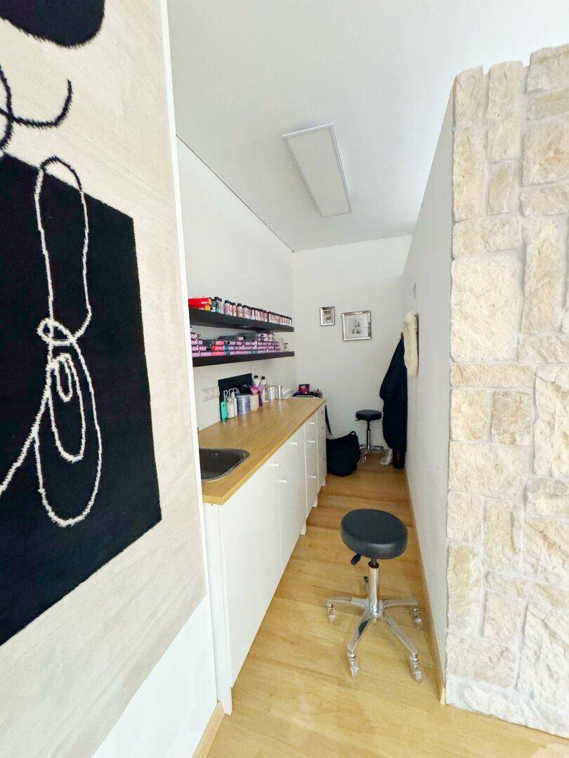 Schmaler Arbeitsbereich mit Holztheke, Spülbecken und Regalen für Produkte im Salon.