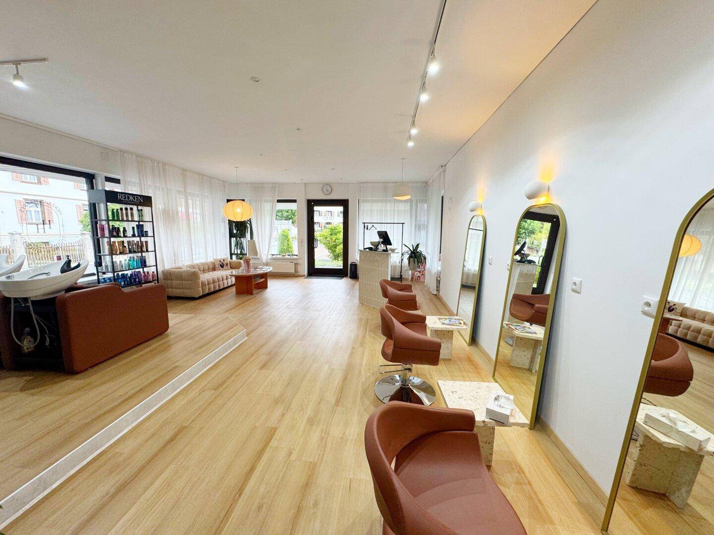 Blick durch den modernen Friseursalon mit mehreren Arbeitsplätzen, großen Spiegeln und Produktregalen.