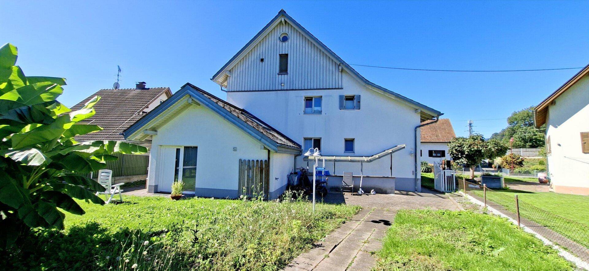 Hinteransicht des Hauses mit großem Gartenbereich und einem Anbau unter blauem Himmel.