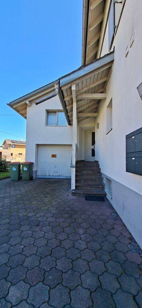 Eingangsbereich des Hauses mit überdachtem Zugang, Treppe und einer Garage mit gepflasterter Fläche.