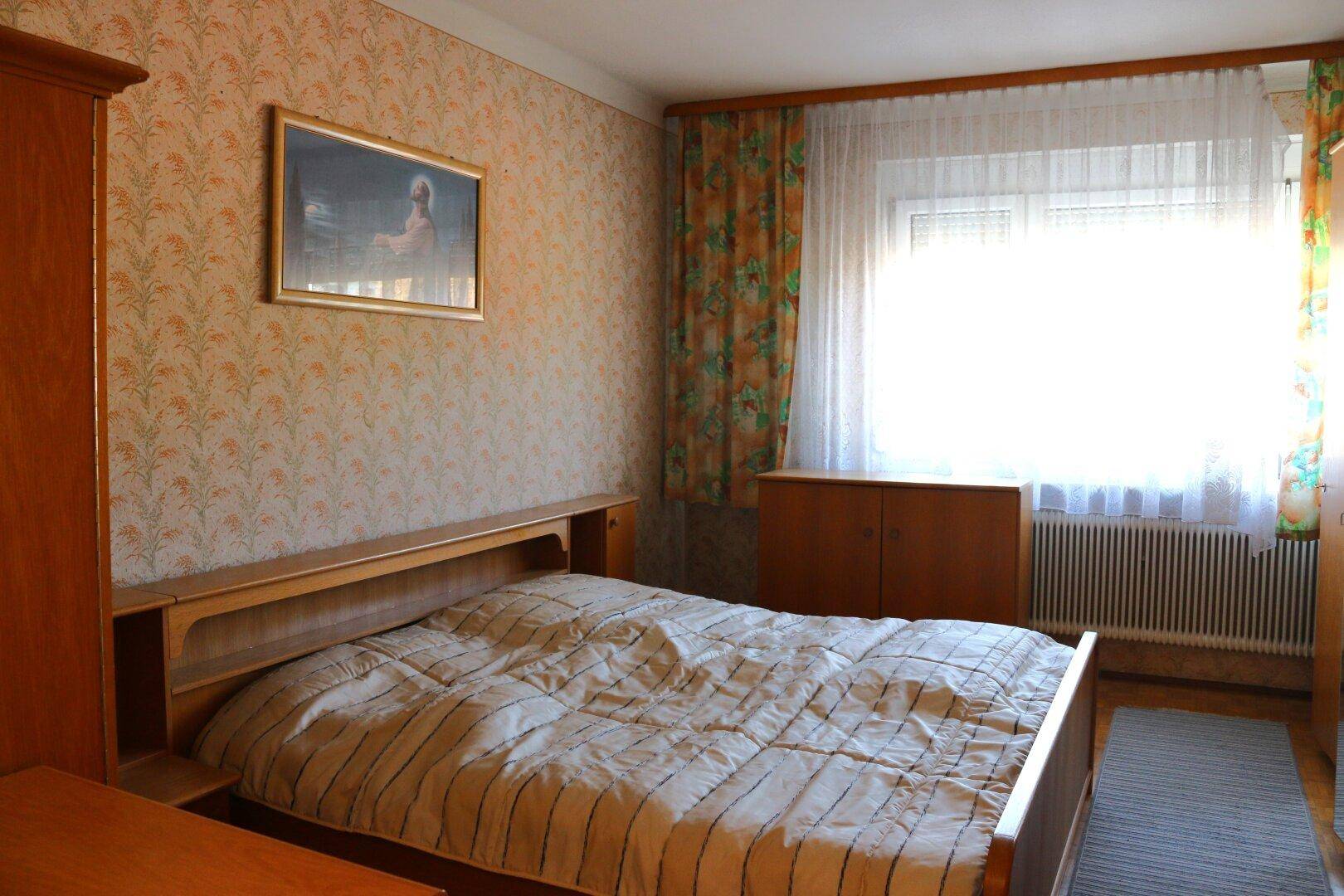 Schlafzimmer mit Doppelbett, Holzmöbeln und gemusterter Tapete.