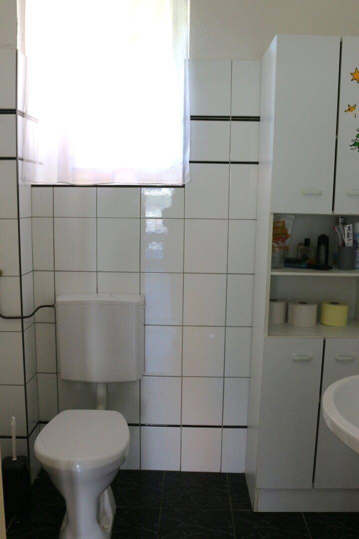 Kleines WC mit Fenster, weißen Fliesen und dunklem Boden.