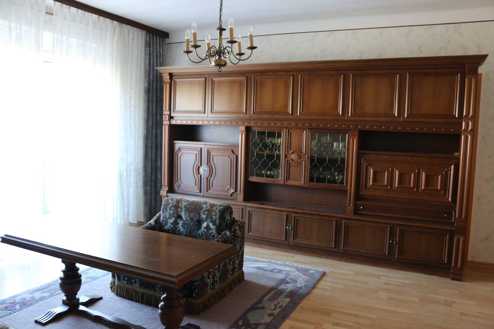Geräumiges Wohnzimmer mit großer Holzschrankwand, Kronleuchter und Parkettboden.