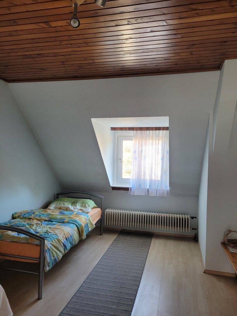 Dachgeschoss-Schlafzimmer mit Einzelbett, Holzdecke und schrägen Wänden.