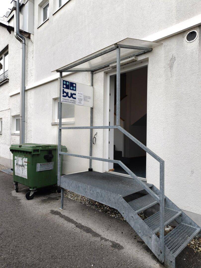 Eingangsbereich eines Gebäudes mit einer Metalltreppe und einem Vordach.
