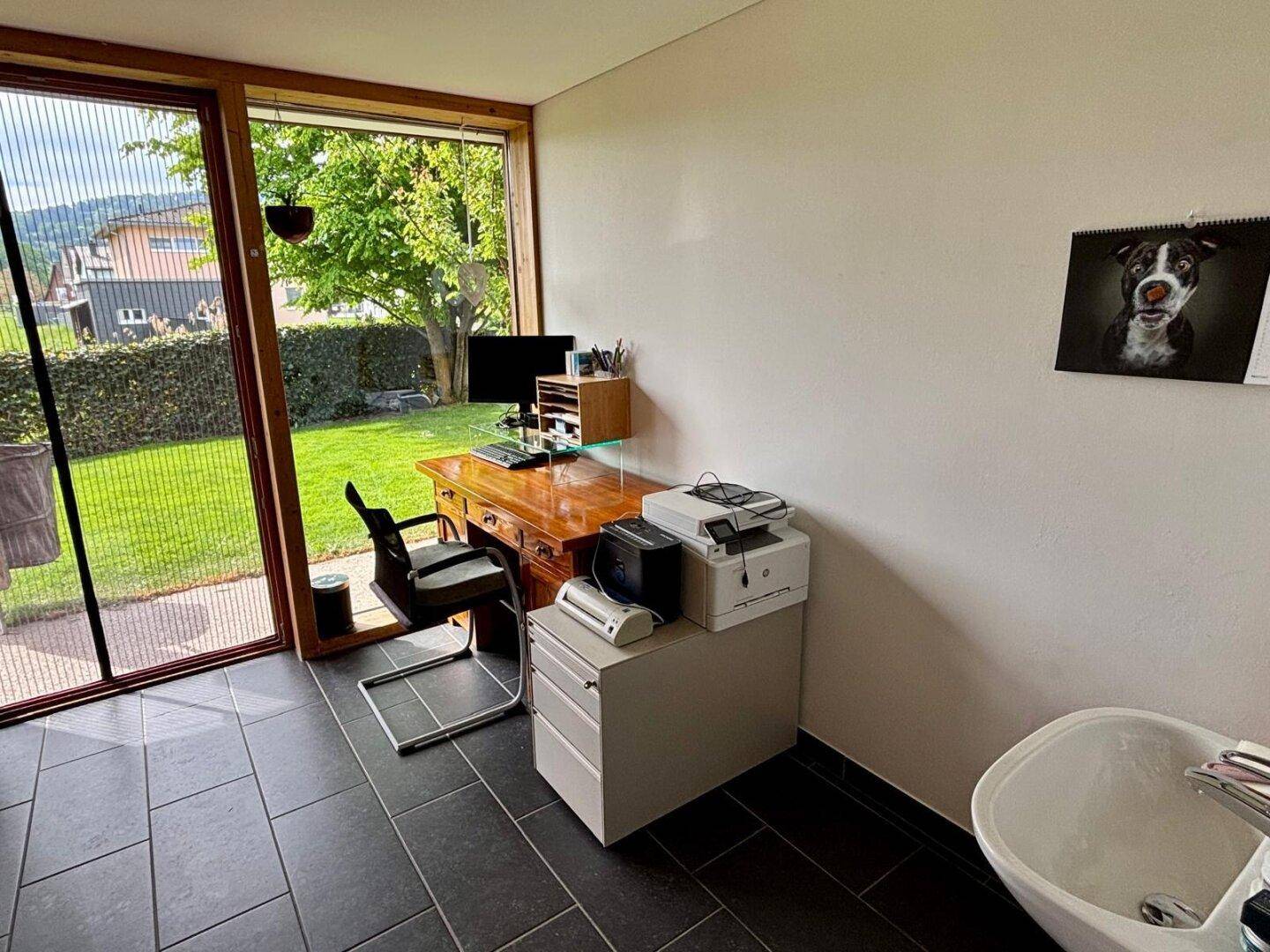 Helles Büro mit großem Fenster und Blick in den Garten, ausgestattet mit einem Schreibtisch.