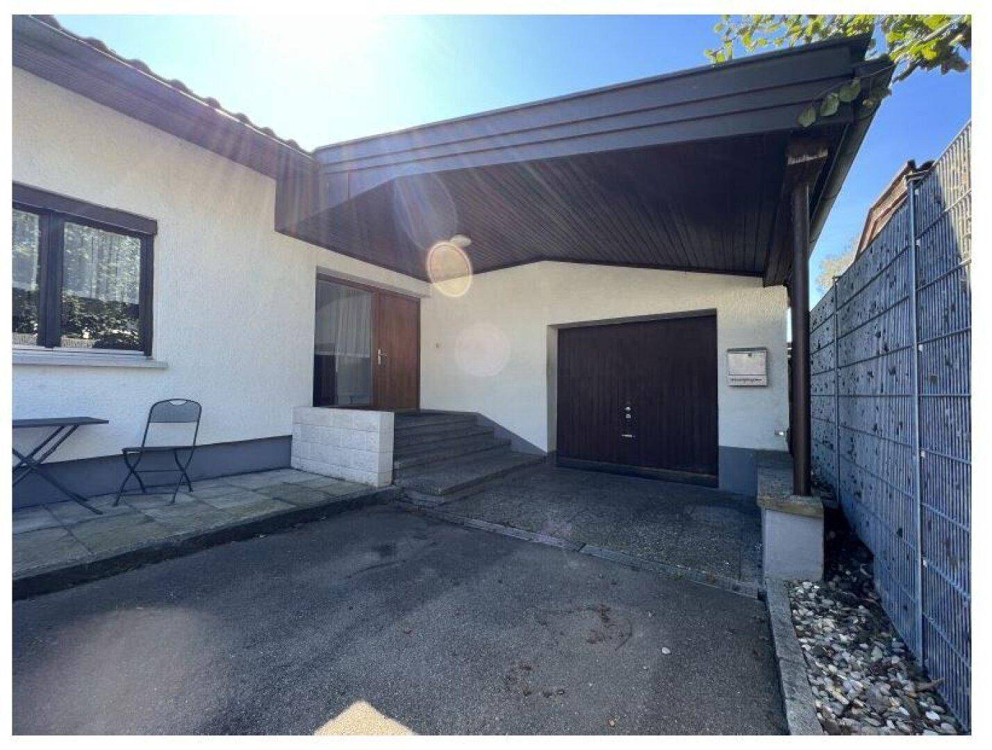 Eingangsbereich des Hauses mit überdachtem Carport und integrierter Garage unter hellem Sonnenlicht.