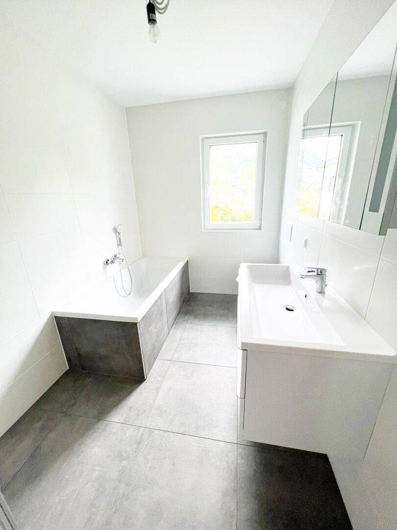 Modernes Badezimmer mit Badewanne, Einzelwaschbecken und Fenster für natürliches Licht.