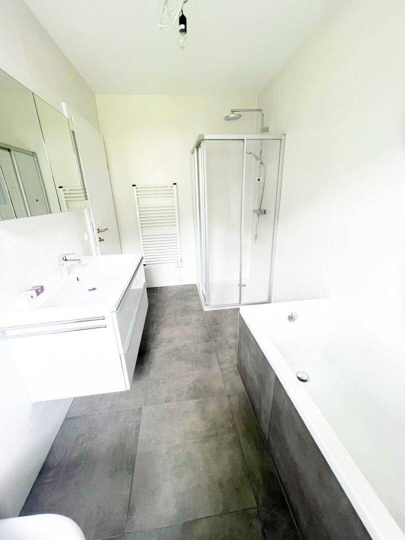 Helles Badezimmer mit Dusche, Badewanne, Einzelwaschbecken und beheiztem Handtuchhalter.
