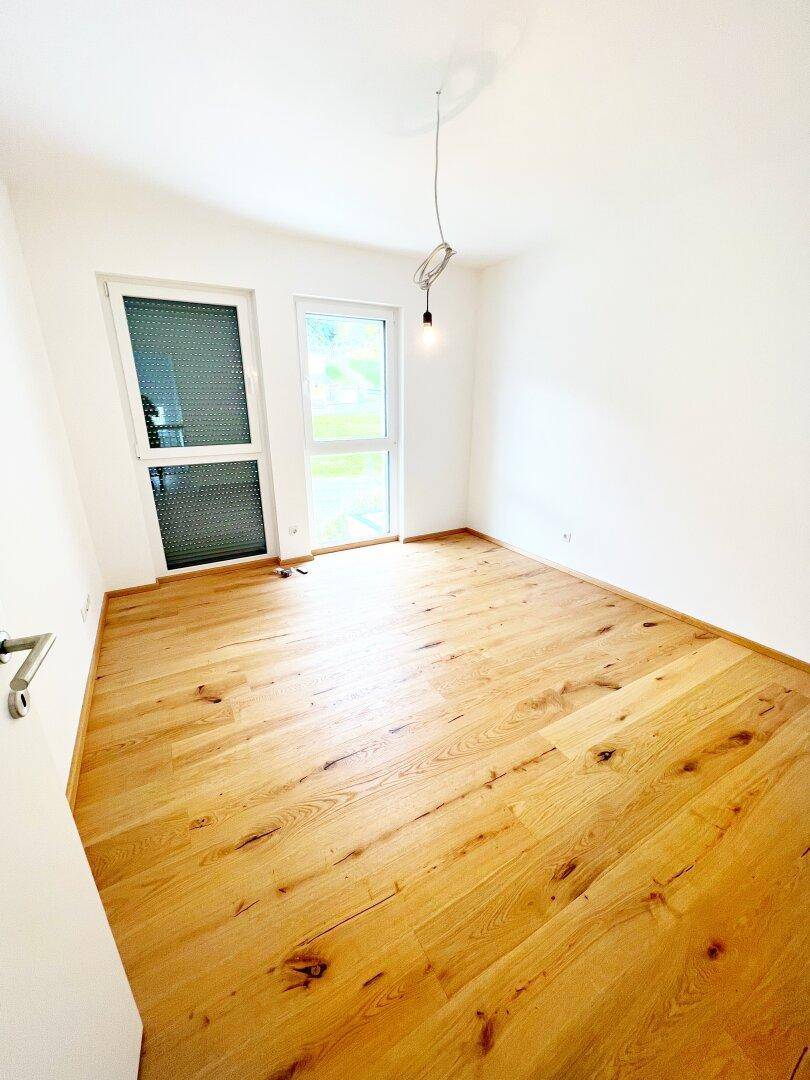 Freundliches Zimmer mit Holzboden und Fenster mit Blick ins Grüne.