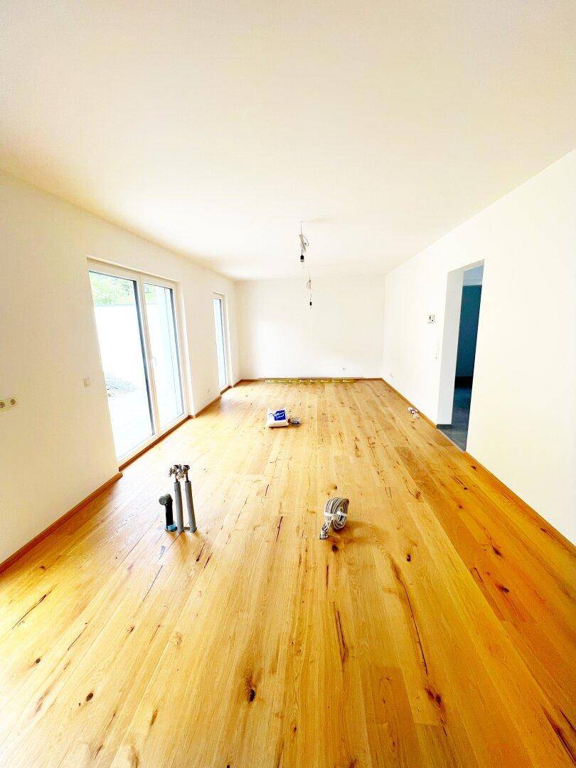 Geräumiger Wohnbereich mit neu verlegtem Holzboden und großen Schiebetüren zur Terrasse.