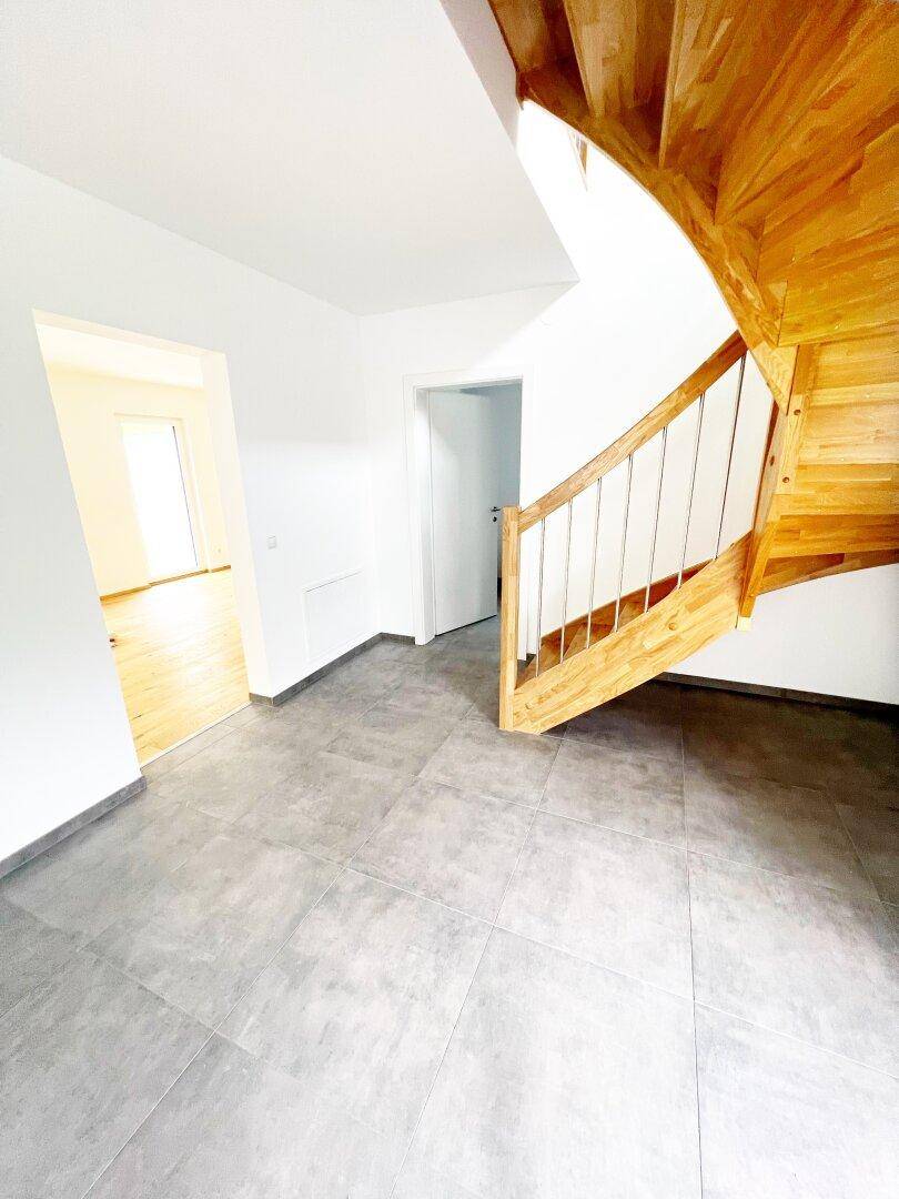 Heller Eingangsbereich mit moderner Holztreppe und Fliesenboden.