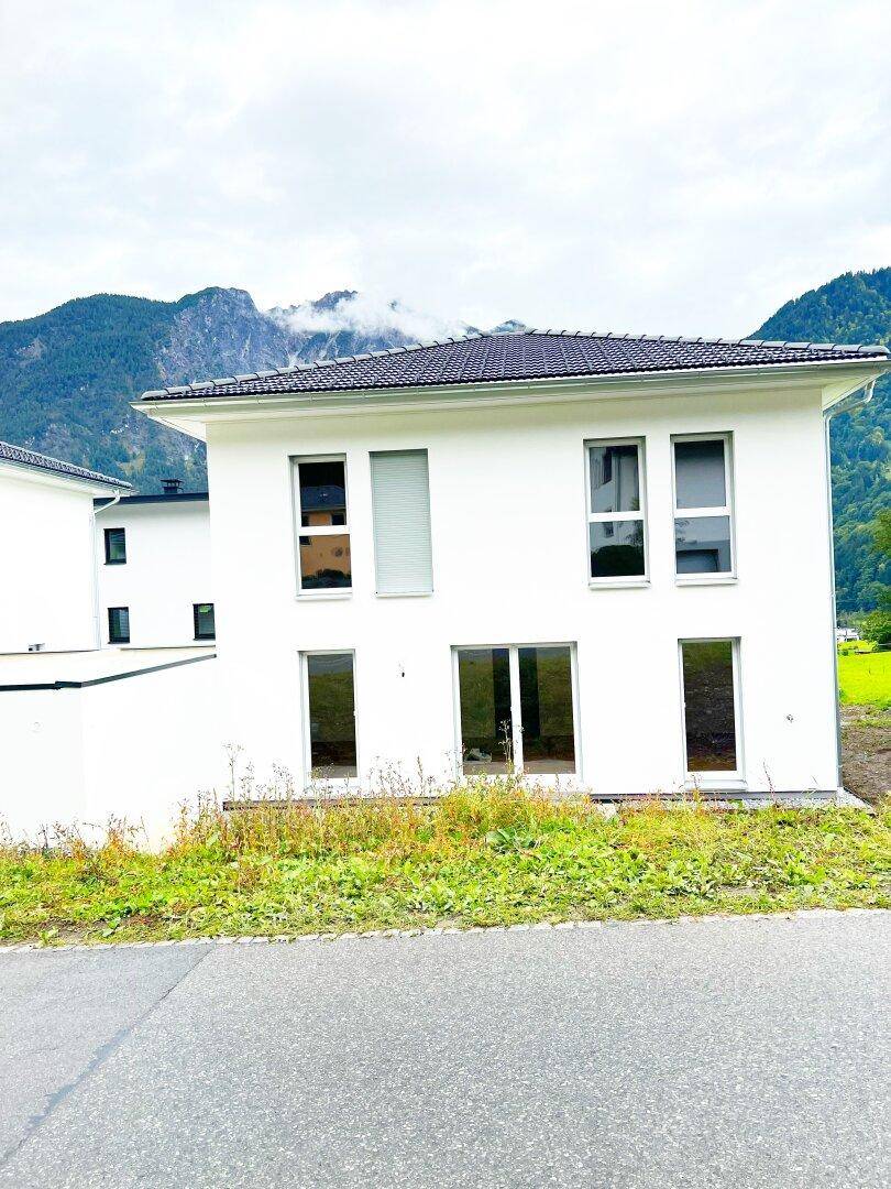 Vorderansicht des modernen Neubaus mit großen Fenstern und Blick auf die Berge im Hintergrund.