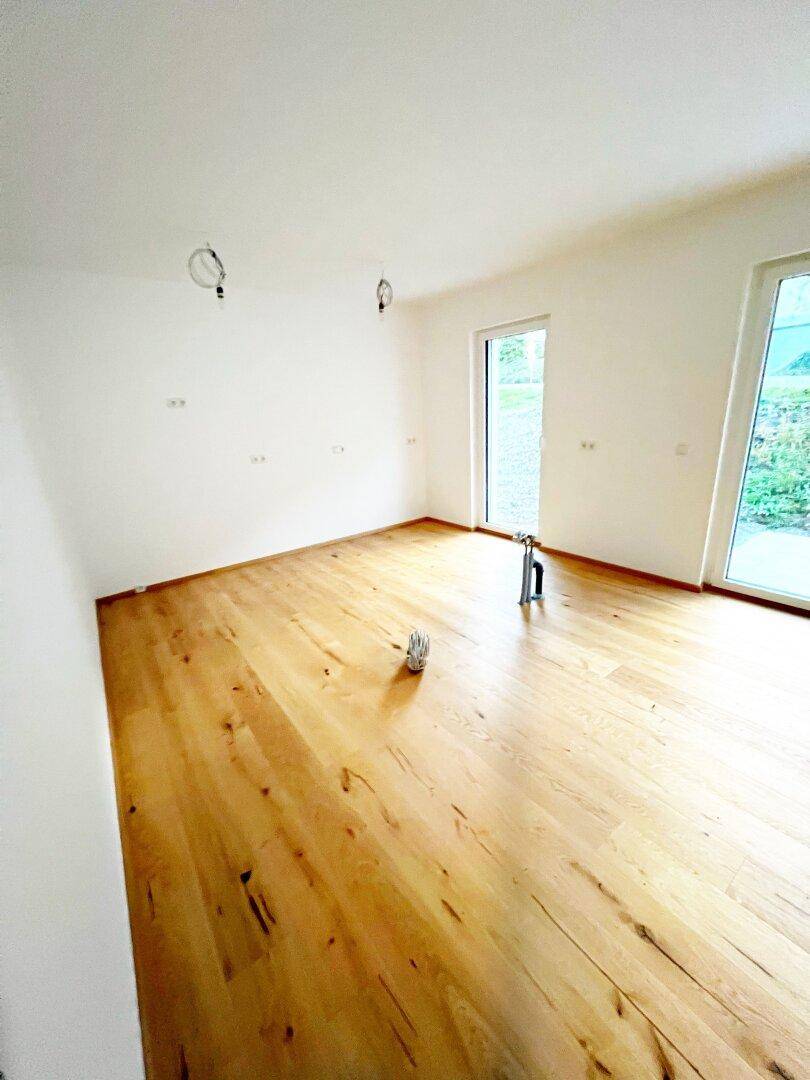 Helles Zimmer mit Holzboden und großen Fenstern, die viel Tageslicht hereinlassen.