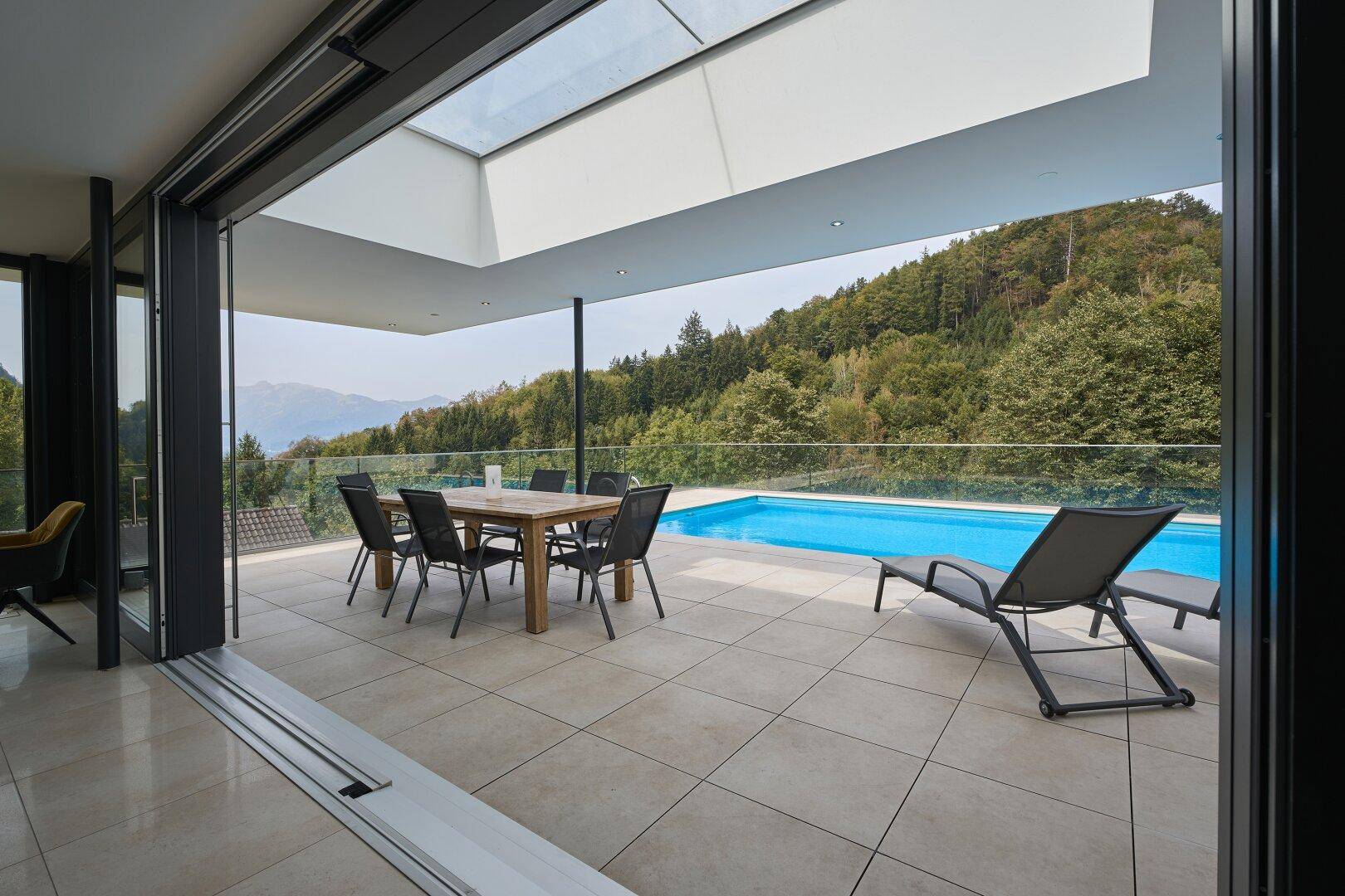 Geräumige Terrasse mit Esstisch, Liegestühlen und Infinity-Pool mit Bergblick.