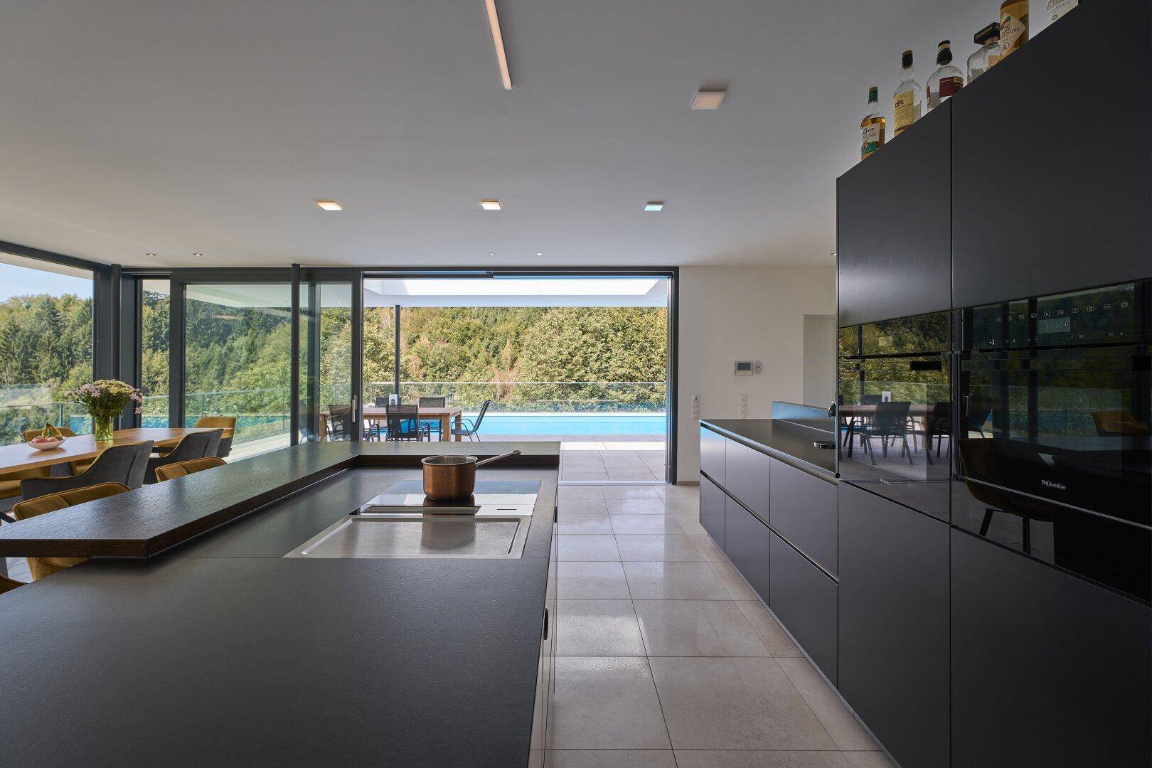 Elegante schwarze Küche mit Kochinsel, modernen Geräten und Blick auf den Pool.