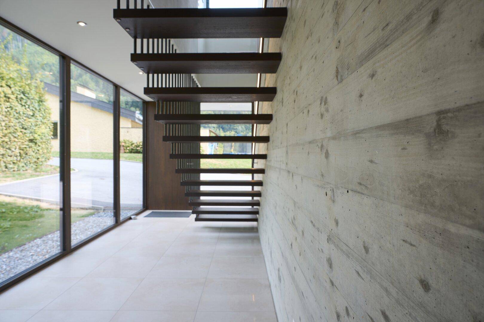 Heller Eingangsbereich mit moderner Holztreppe und Sichtbetonwand.