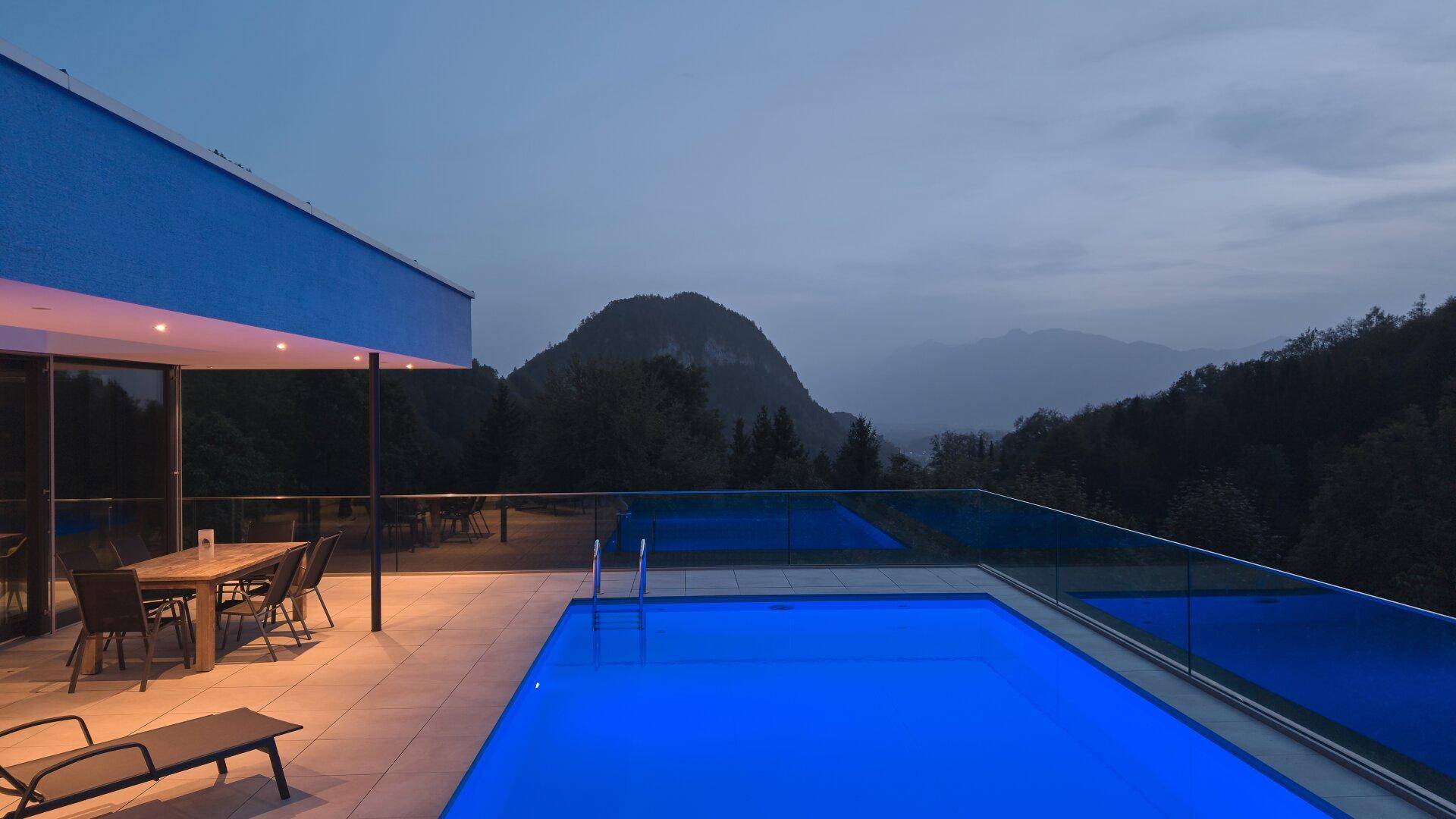 Beleuchteter Infinity-Pool und Terrasse bei Dämmerung mit malerischem Bergblick.