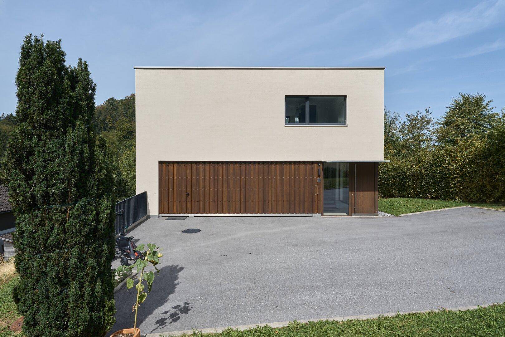 Moderne Hausfassade mit Holzgarage und Eingangsbereich, umgeben von Grün.