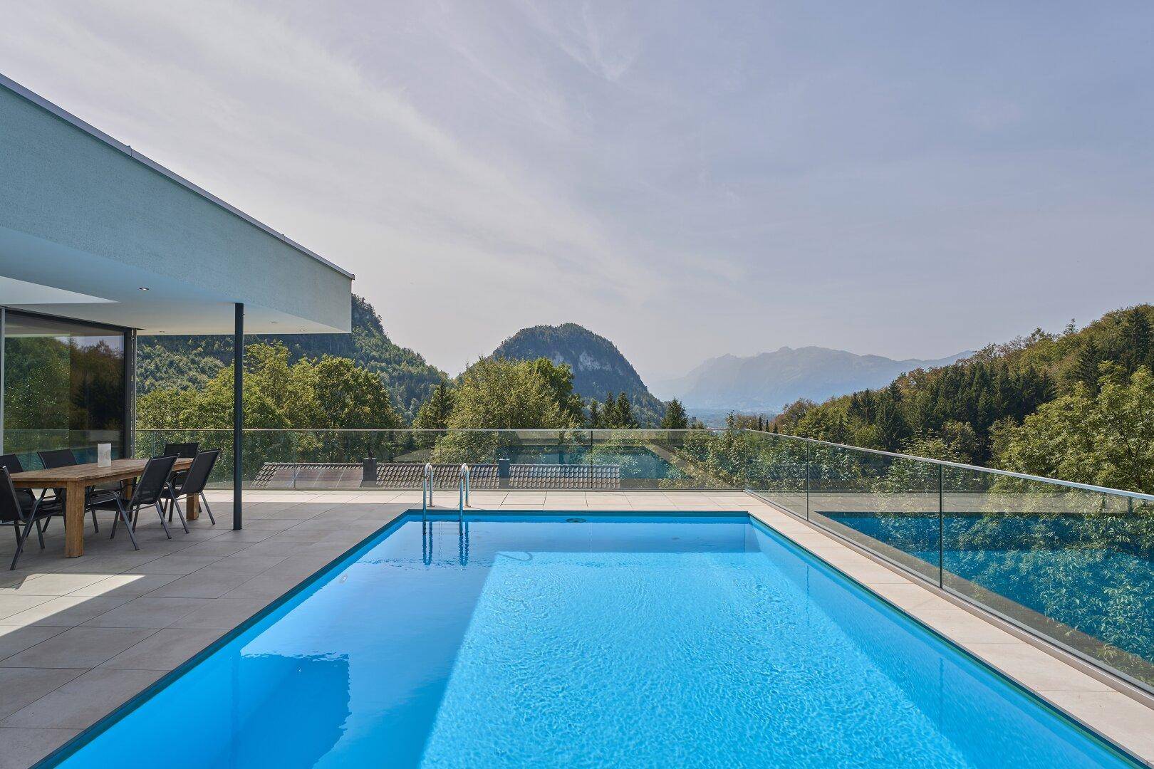 Blauer Infinity-Pool mit atemberaubendem Bergblick unter klarem Himmel.