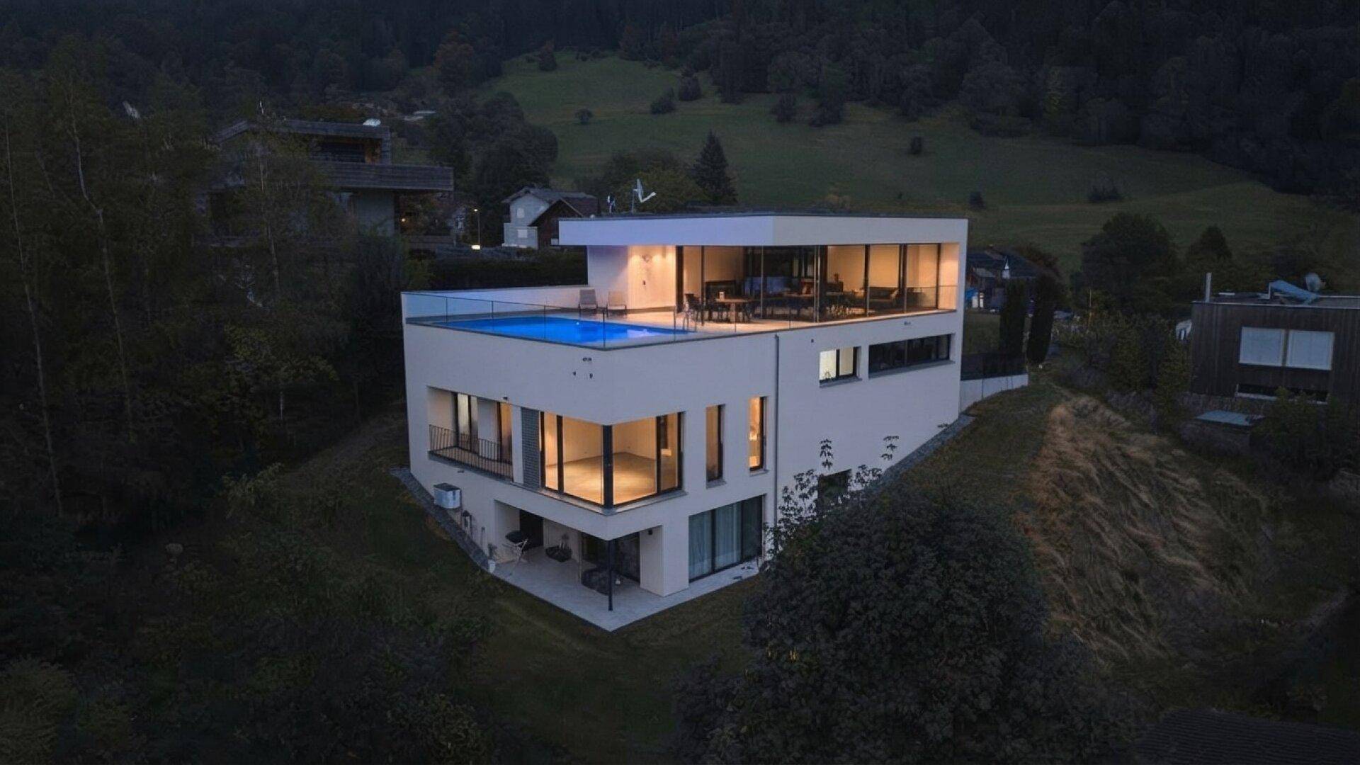 Moderne Villa bei Dämmerung, mit beleuchteten Innenräumen und Dachpool.