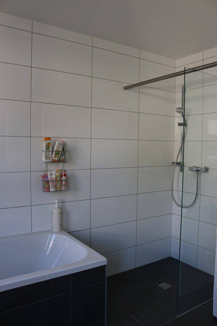 Modernes Badezimmer mit Badewanne, Duschbereich und weißen Fliesen.