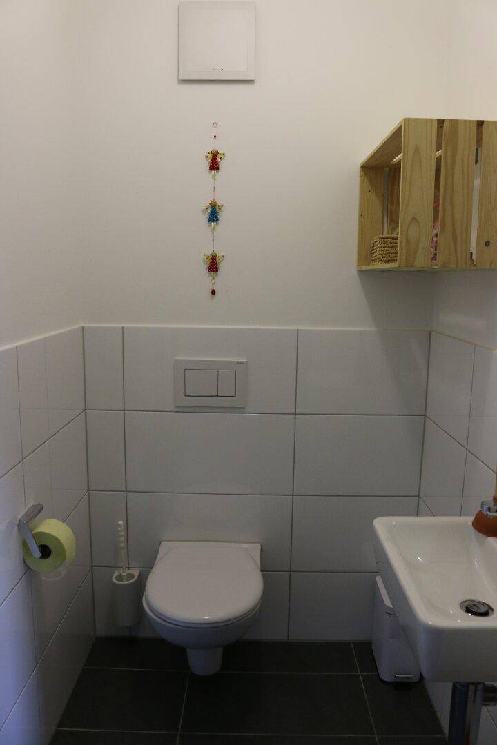 Separates Gäste-WC mit Wand-WC, kleinem Waschbecken und weißen Fliesen.