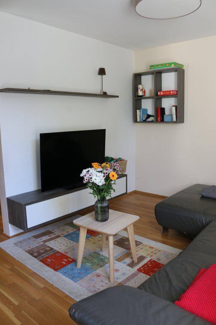 Wohnzimmer mit Fernseher, modernem Sideboard und hellem Holzboden für entspannte Abende.